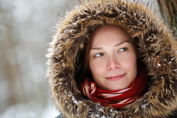 Женщина в снежном зимнем лесу с шеей и красным шарфом улыбается — стоковое фото