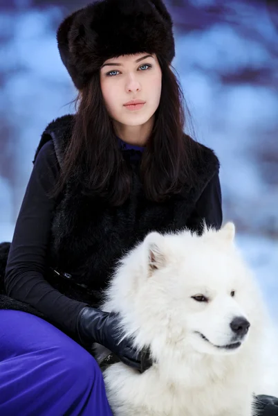 Young beautiful woman in fur hats in winter forest with dog — Stock Photo, Image