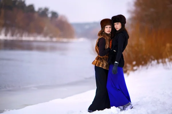 Two young beautiful women in fur hats in winter forest near rive — Stock Photo, Image