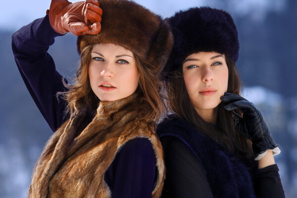 Two young woman in fur hats in winter forest