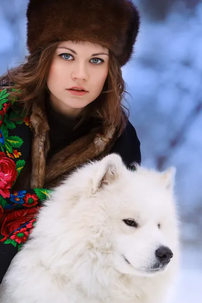 Ung vacker kvinna i päls hattar i vinter skog med hund samo Stockbild