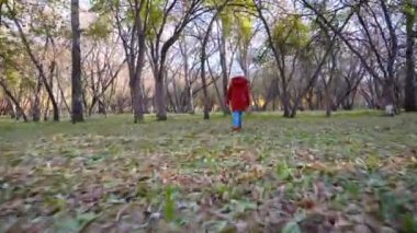 Şapkalı ve ceketli mutlu bir kız çocuğu sonbahar ormanında turuncu yapraklarla koşar ve ellerini sallar. Parkta veya meydanda sonbahar yürüyüşü yapar. Çocukluğunda tasasız bir çocukluk.