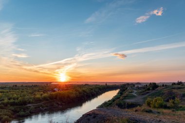 Nehir ve ormanın üzerindeki ilahi güneş ışığı. Güneşin bulutları ve ışınlarıyla dramatik akşam gökyüzü. Akşam gün batımında ya da sabah güneşinde altın saat.