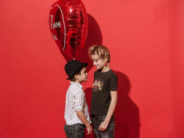 Meisje en jongen met rood ballon op de rode achtergrond, zijn ze glimlachen en proberen om elkaar kussen. — Stockfoto