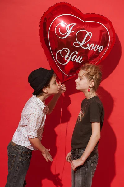 女の子と男の子の赤の背景に大きな心のこもったバルーン。笑顔され、お互いにキスをしようとしています。 — ストック写真