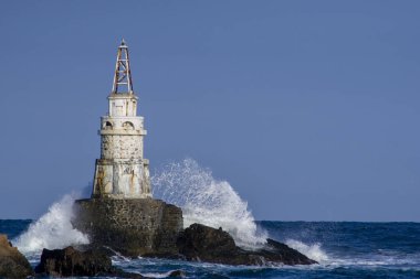 Gün batımında mavi saatte deniz fenerine dalgalar çarpar.