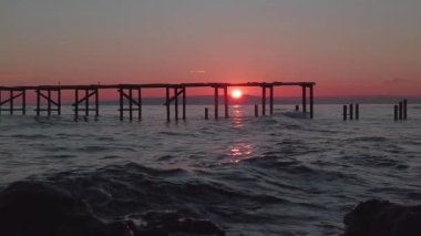 Gün batımında ıssız bir sahilde terk edilmiş bir iskele.