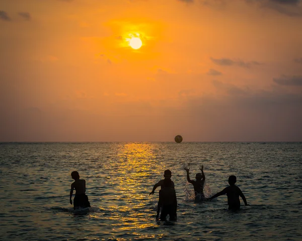 Silueta grupo de chicos están jugando una pelota en el mar —  Fotos de Stock