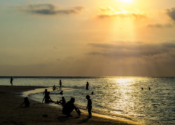 Silhouetted group of people on the beach and in the sea — Stock Photo, Image