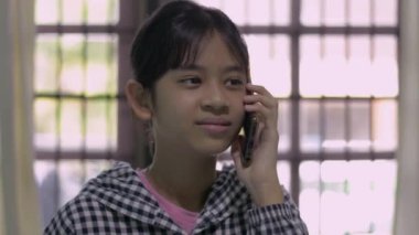 Sıradan elbiseli Asyalı güzel kız evde arkadaşıyla mutlu bir şekilde konuşuyor. Telefonda konuşurken gülümseyen ve gülen sevimli genç kız portresi..