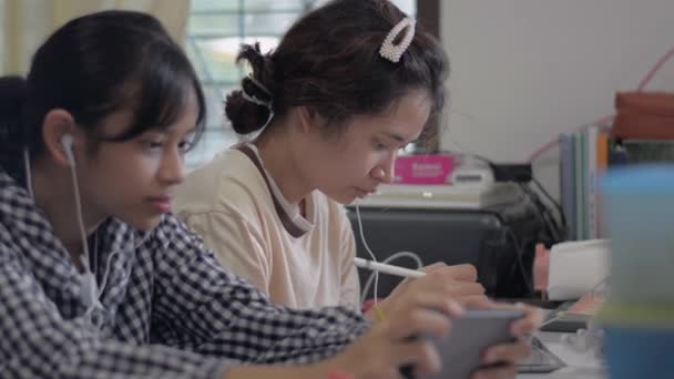 亚洲漂亮的少女在网上学习课程 桌上挂着数字平板电脑 而她的妹妹则喜欢在家里用耳机玩网络游戏 家人团聚在一起 — 图库视频影像
