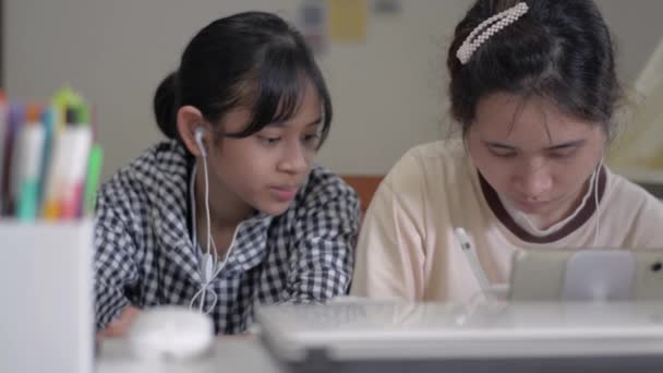 亚洲可爱的两姐妹与数码平板电脑和耳机一起在家里的办公桌上工作 家庭隔离期间 学生在通信技术装置上的协作学习 — 图库视频影像