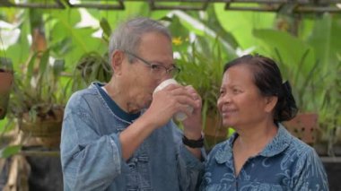 Sağlıklı son sınıf çifti sıcak içecekten ve evdeki bahçede dikilirken kameraya bakmaktan zevk alır. Mutlu emekli büyükanne ve büyükbaba portresi. Yaşlılara duyulan sevgiyle bağlanmak.