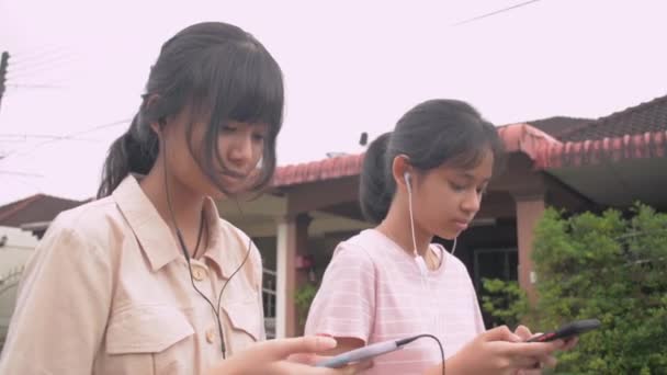Två Asiatiska Tonårstjejer Bär Hörlurar Som Sms Sociala Medier Online — Stockvideo