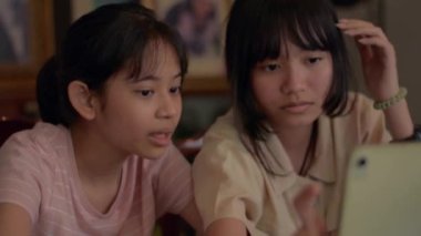 İki Asyalı sevimli kız kardeş evlerinde dijital tablet üzerinde fotoğraf uygulamalarıyla eğleniyorlar. Mutlu Taylandlı genç kızlar dijital cihazda internetten sosyal video görüşmelerini seviyorlar. Kardeş ve genç yaşam tarzı.