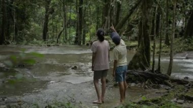 Mutlu Asyalı anne ve genç kızı sabah yeşil bitkilerin arasından akan su akıntısı ile tropikal ormanın güzel manzarasının keyfini çıkarıyorlar. Phang Nga Eyaleti. Tayland.