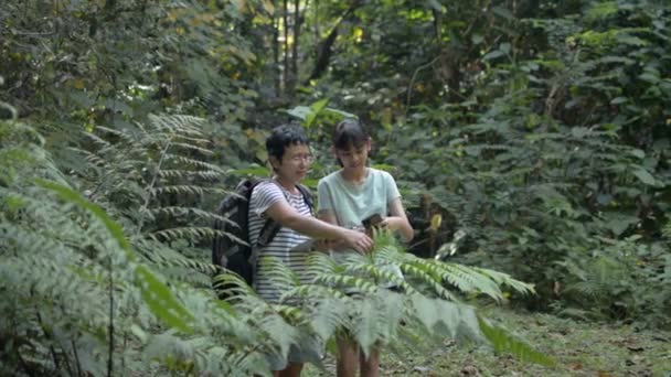 背着背包的亚洲生物学家妈妈正在向她十几岁的女儿解释森林里的热带植物 丛林里的户外探险自然保护 泰国徒步旅行 — 图库视频影像