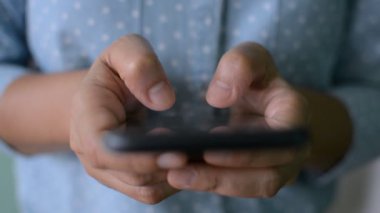 Mavi tişörtlü, cep telefonunun dokunmatik ekranına yazı yazan bir kadının ellerini kapat. Mobil uygulama üzerinden mesaj gönderiliyor. Çevrimiçi sosyal iletişim üzerine sohbet. 