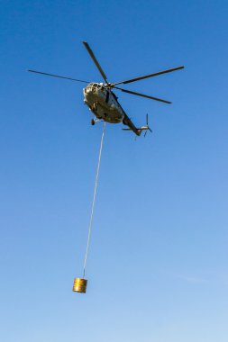 Helicopter in action carrying the water bucket. Shot from the ground. clipart