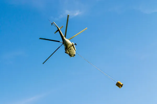 Helicóptero em ação carregando o balde de água. Tiro a partir do abaixo . — Fotografia de Stock