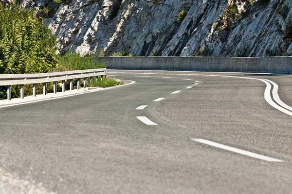 Strada asfaltata sinuosa con rocce in pietra sullo sfondo . — Foto Stock