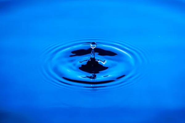 Ondas de água causadas pela queda de gotículas com iluminação azul — Fotografia de Stock