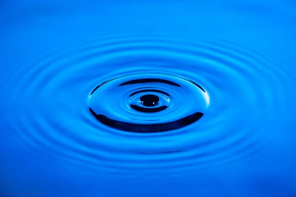 Waves of water caused by the falling droplets with blue lighting — Stock Photo, Image