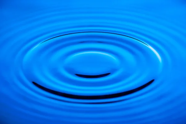 Vågor av vatten orsakas av fallande droppar med blå belysning — Stockfoto