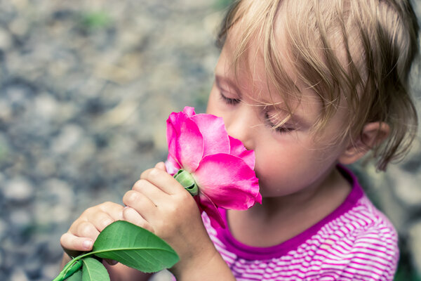 Beautiful greeting child smelling a rose