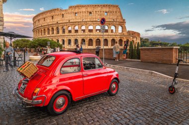 Roma, İtalya 17.07.2021: Küçük kırmızı Fiat 500 gün batımında kolezyumun önünde ve arkasında piknik sepeti ile