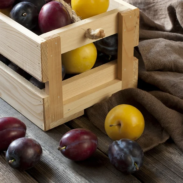 Ciruelas frescas en caja sobre tabla de madera — Foto de Stock