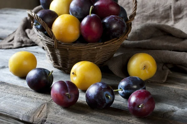 Still life with plums in a basket on the table — Stock Photo, Image