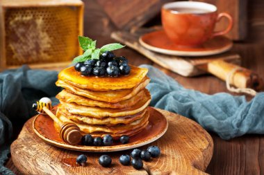 Böğürtlenli küçük ev yapımı krepler, çay fincanı ve ahşap masa üzerinde bal peteği.