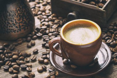 Ahşap arka planda kahve fincanı ve kahve çekirdekleri, sığ alan derinliğinde seçici odak