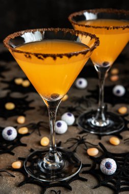 Cadılar Bayramı turuncu kokteyli. İçki konsepti, karanlık arka planda tatil süslemeleri olan bardaklar.