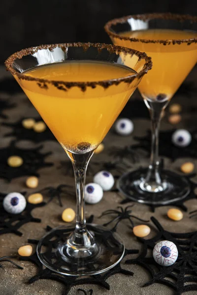 Cadılar Bayramı turuncu kokteyli. İçki konsepti, karanlık arka planda tatil süslemeleri olan bardaklar.