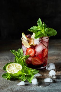 Limonlu, çilekli, koyu beton arka planda nane yapraklı, seçici odaklı içecek.