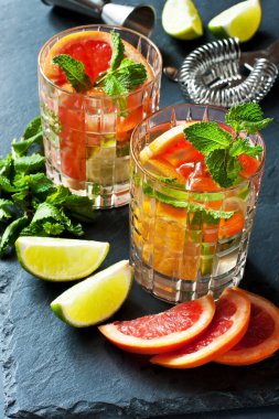 Koyu beton arka planda limon, portakal, greyfurt ve nane yapraklarıyla taze içecek, seçici odaklanma