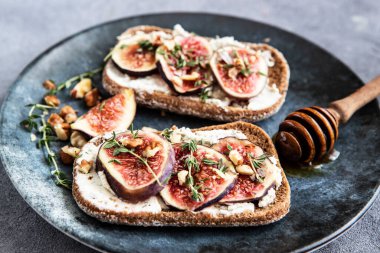 Toasted baguette with cream cheese, figs and thyme on ceramic plate, selective focus