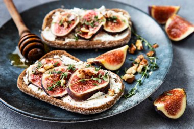 Toasted baguette with cream cheese, figs and thyme on ceramic plate, selective focus