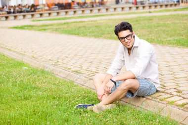 kaldırımda oturan ve kameraya gülümseyen yakışıklı adam