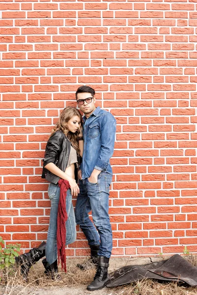 Atraente casal elegante casualmente encostado contra a parede de tijolo — Fotografia de Stock