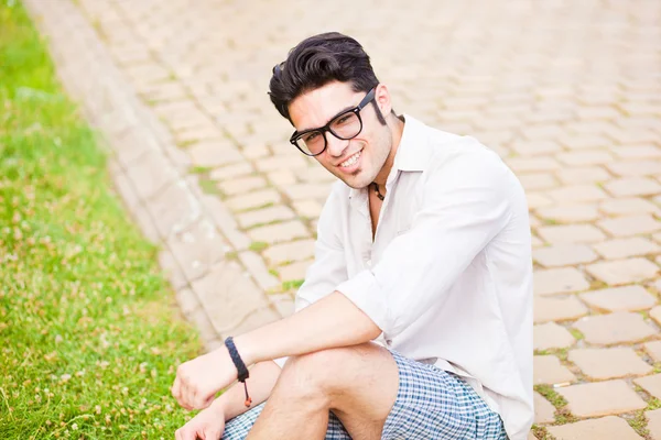 Hombre guapo sentado en la acera y sonriendo a la cámara —  Fotos de Stock