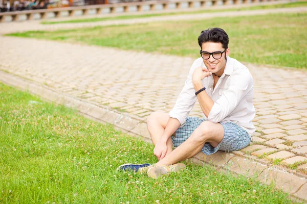 Przystojny mężczyzna siedzi na chodniku i uśmiechając się do kamery — Zdjęcie stockowe