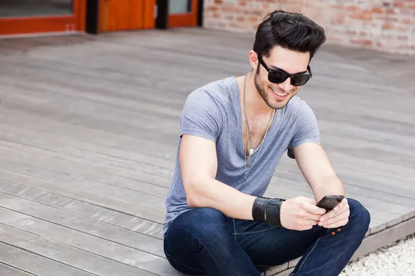 Ελκυστικό νεαρό αρσενικό μοντέλο γραπτών μηνυμάτων σε ένα smartphone — Φωτογραφία Αρχείου