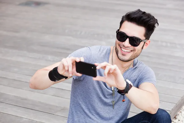 Atractivo modelo masculino tomar fotos con un teléfono inteligente negro —  Fotos de Stock