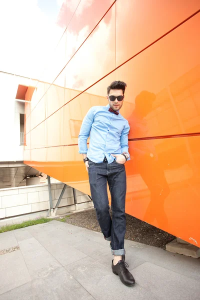 Красивый молодой мужчина-модель позирует на открытом воздухе в голубой рубашке и солнечных очках — стоковое фото
