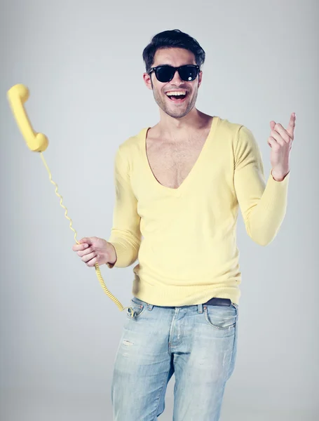 Homem atraente sorrindo e brincando com um telefone amarelo — Fotografia de Stock