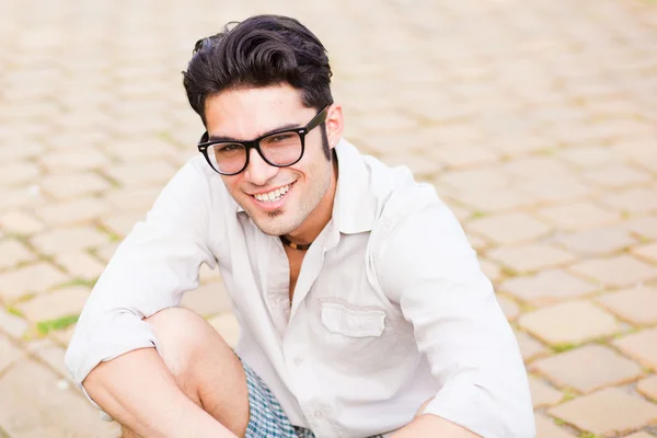 Handsome man wearing glasses sitting on the sidewalk and smiling Royalty Free Stock Photos