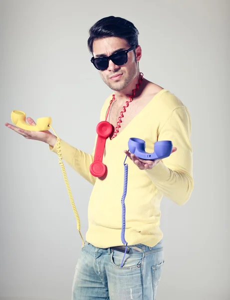 Guapo y divertido chico con gafas hipster y teléfonos de colores Imagen de stock